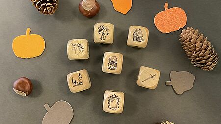 Es sind sieben Würfel mit mythischen und alltagsgebräuchlichen Wesen und Gegenständen zu sehen. Drumherum wurde herbstlich dekoriert mit Tannenzapfen, aus Pappe herausgeschnittenen Kürbissen und Nüssen und Kastanien befinden sich dort.