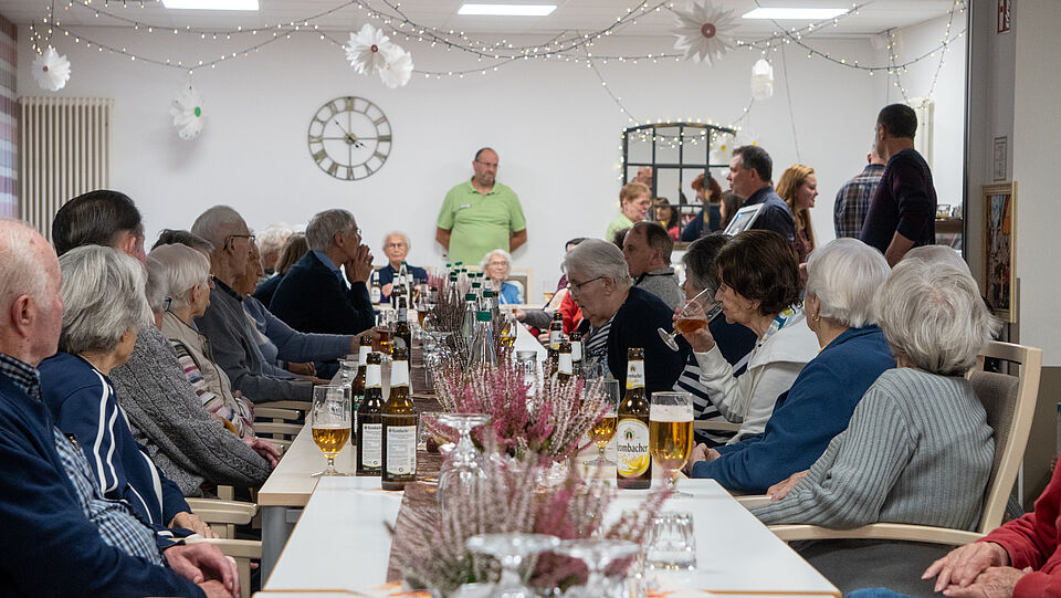 Eine Gruppe von Seniorinnen und Senioren sitzen an einer langen Tafel und hören dem Redner aus der Ukraine zu.