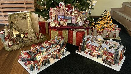 Geschenke vom Christkind, die vor einem Weihnachtsbaum stehen. Es sind bunt eingepackte Geschenke und ein Adventskalender zu sehen.